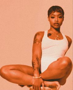 a woman sitting on top of a stool with her leg up in the air while wearing a white tank top