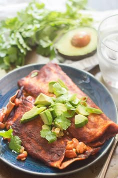 an enchilada on a plate with avocado and cilantro