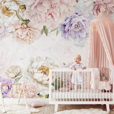 a baby sitting in a crib next to a wall with flowers painted on it