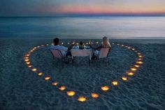 two people sitting at a table in the shape of a heart with candles on it