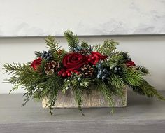 a wooden box filled with red flowers and pine cones sitting on top of a table