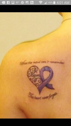 the back of a woman's shoulder with a purple ribbon and heart tattoo on it