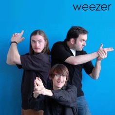 three people standing in front of a blue wall with the words weezer on it