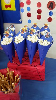 there are some cones that have popcorn in them on top of a blue table cloth