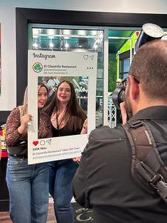 a man taking a photo of two women in front of a store window with an instagram sign