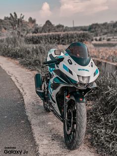 a white and blue motorcycle parked on the side of a road next to tall grass