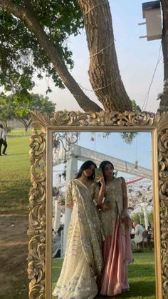 two women standing next to each other in front of a large mirror on the grass