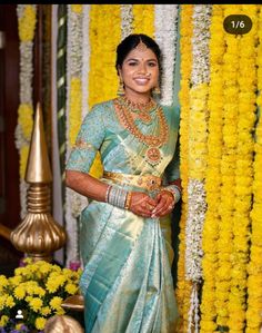 a woman in a blue and gold sari posing for the camera with yellow flowers behind her