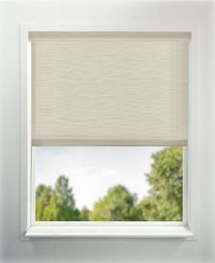 a window with a white roller shade in front of the windowsill and trees behind it