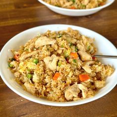 two white bowls filled with chicken and rice on top of a wooden table next to each other