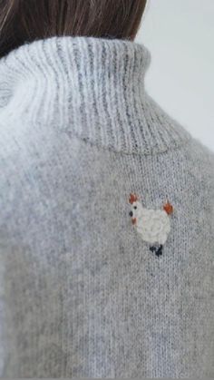 a woman wearing a gray sweater with an embroidered chicken on it