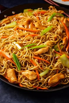 noodles with chicken, carrots and green onions in a wok on a table