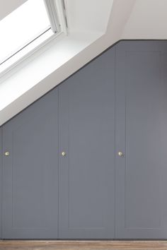 an empty room with gray cupboards and wooden floors in the corner, under a slanted roof