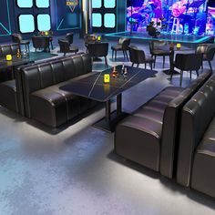 a room filled with lots of black couches and tables in front of a large screen