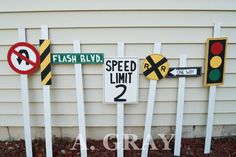 several street signs and traffic lights on white poles in front of a house with grass