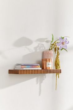 a wooden shelf with flowers and books on it next to a wall mounted candle holder