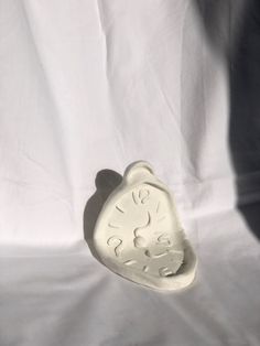 a white ceramic clock on a white sheet with shadow from the person's hand