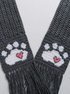 two gray crocheted scarfs with hearts and paw prints on them, one has a red heart in the middle