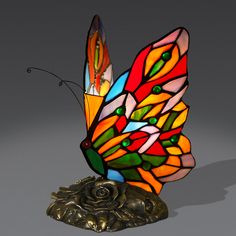 a stained glass butterfly sitting on top of a metal base with a rose in it's center