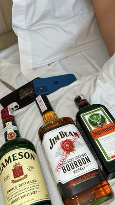 three bottles of alcohol sitting on top of a bed