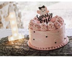 a pink birthday cake sitting on top of a table next to a number one sign