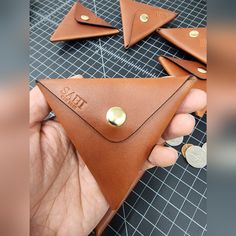 a hand holding a leather wallet with gold buttons on it and three other pieces in the background