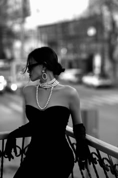 black and white photograph of woman in evening dress with pearls on her neck, looking down at the street