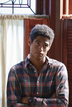 a young man standing in front of a window with his arms crossed and looking at the camera