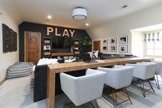 a living room filled with furniture and a long table in front of a tv mounted on the wall