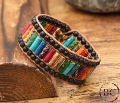 two leather bracelets with multicolored beads are sitting on a piece of wood