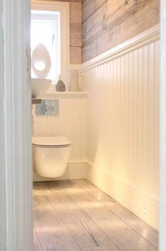 a white toilet sitting inside of a bathroom next to a wooden wall and flooring