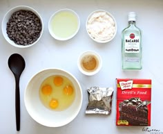 ingredients to make chocolate cake laid out on a white counter top, including eggs, milk, and flour