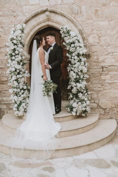 a bride and groom standing in front of an arch with flowers on it at their wedding