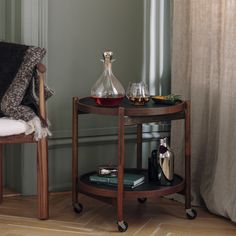 a table with two glasses and a bottle on it next to a chair in front of a window