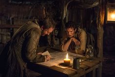 two men sitting at a table with a lit candle in front of them on paper