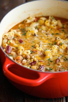 a red pot filled with macaroni and cheese soup on top of a wooden table