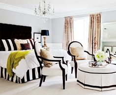 a bedroom with black and white bedding, chandelier, two chairs and a coffee table