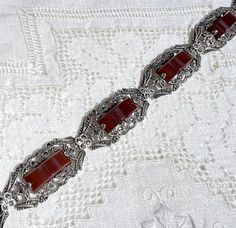 "This lovely Art Deco bracelet, composed of genuine carnelian, marcasites, and sterling, was made in Germany.  Every link has a  carnelian stone was a curved top.  The color of the carnelian is a dark brownish reddish orange.  Each link that is set with a carnelian stone shows an open-work design and is studded with marcasites.  The bracelet is further detailed with decorative connector links, which are also studded with marcasites.  There is a hidden tongue-and-box clasp, and it is stamped \"GERMANY STERLING\" on the tongue. The bracelet has a hinged safety for added security. Condition:  Excellent! All marcasites are present. Clasp works fine. Approximate measurements:  7 1/4\" long, 1/2\" wide" Elegant Carnelian Gemstone Bracelets, Art Deco Bracelet, Reddish Orange, Carnelian Stone, Work Design, Box Clasp, Sterling Silver Bracelet, Vintage Art Deco, Chain Link Bracelet