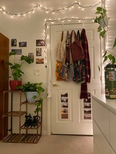 a room with plants and clothes hanging on the wall, next to a white door