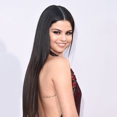 a woman with long hair and tattoos on her back, posing for the camera at an american music awards event