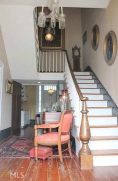 the stairs in this house have chandeliers hanging from them, and there is a pink chair next to it