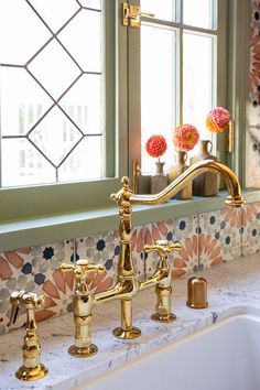 a sink with two faucets in front of a window and flowers on the windowsill