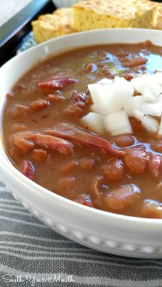 a white bowl filled with beans and onions next to a piece of bread on top of a table