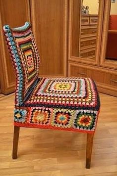 a colorful crocheted chair sitting on top of a hard wood floor next to a mirror