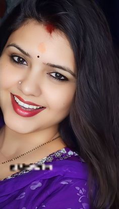 a woman with long black hair wearing a purple sari and smiling at the camera