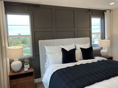 a large bed sitting next to two windows in a bedroom with white and black decor