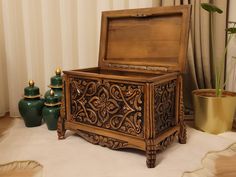 an ornately carved wooden box sits on the floor next to two green vases