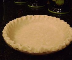 an uncooked pie crust sitting on top of a counter next to some glasses