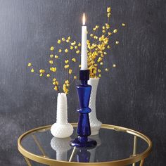 two blue vases with yellow flowers in them on a glass table next to a black wall