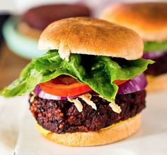 two burgers with lettuce, tomato and onion on them sitting on a plate